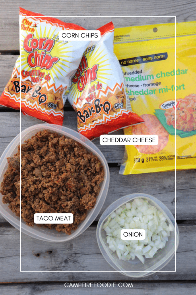 Top-down view of taco ingredients on a wooden surface: two bags of BBQ corn chips, a pack of shredded cheddar cheese, a container of cooked taco meat, and a small container of chopped onions.