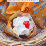 A waffle cone filled with cherry pie dessert, topped with whipped cream and a cherry, sits in a basket among Bear Club Grahams snack packs. Text overlay reads cherry pie WALKING DESSERT and CAMPFIREFOODIE.COM.