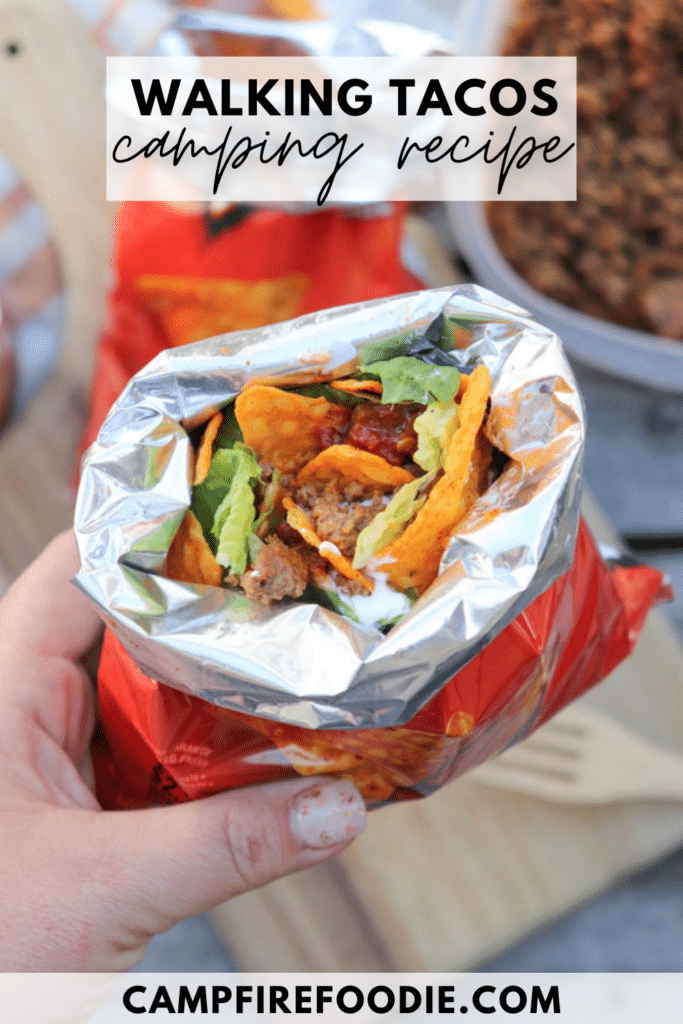 A hand holds an open snack-size Doritos bag filled with taco meat, lettuce, and salsa. Text reads Walking Tacos camping recipe and campfirefoodie.com appears at the bottom.
