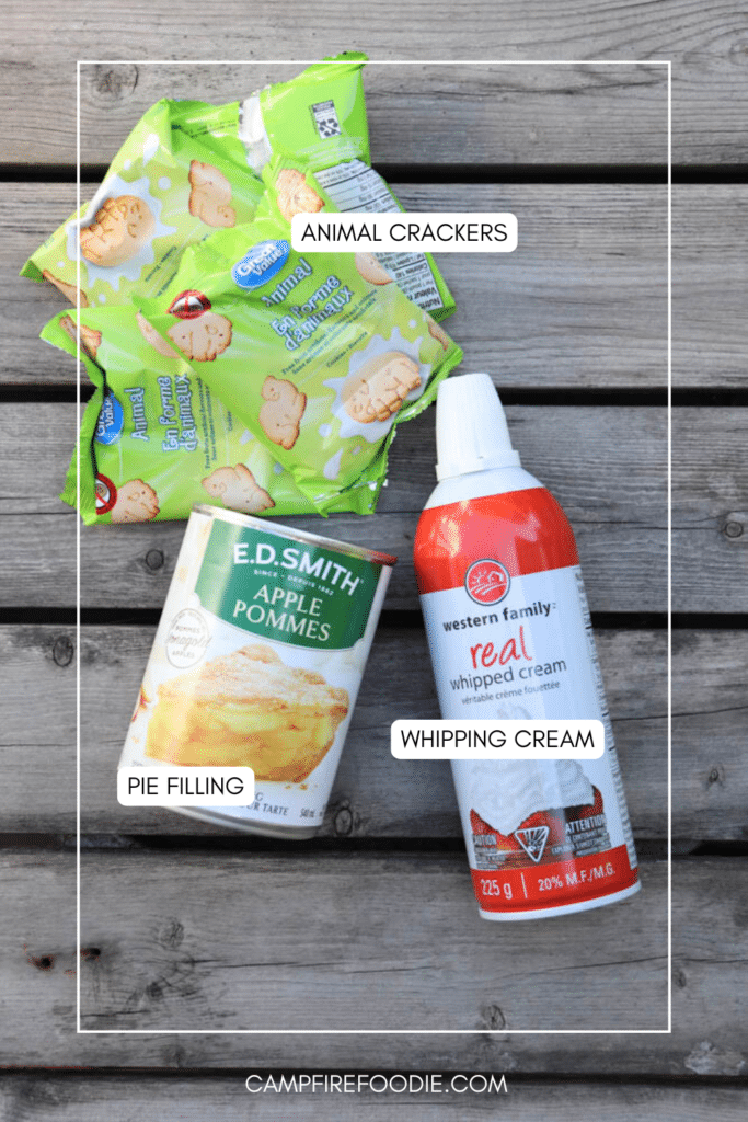 Four packs of animal crackers, a can of apple pie filling, and a can of whipped cream are arranged on a wooden surface, labeled accordingly.