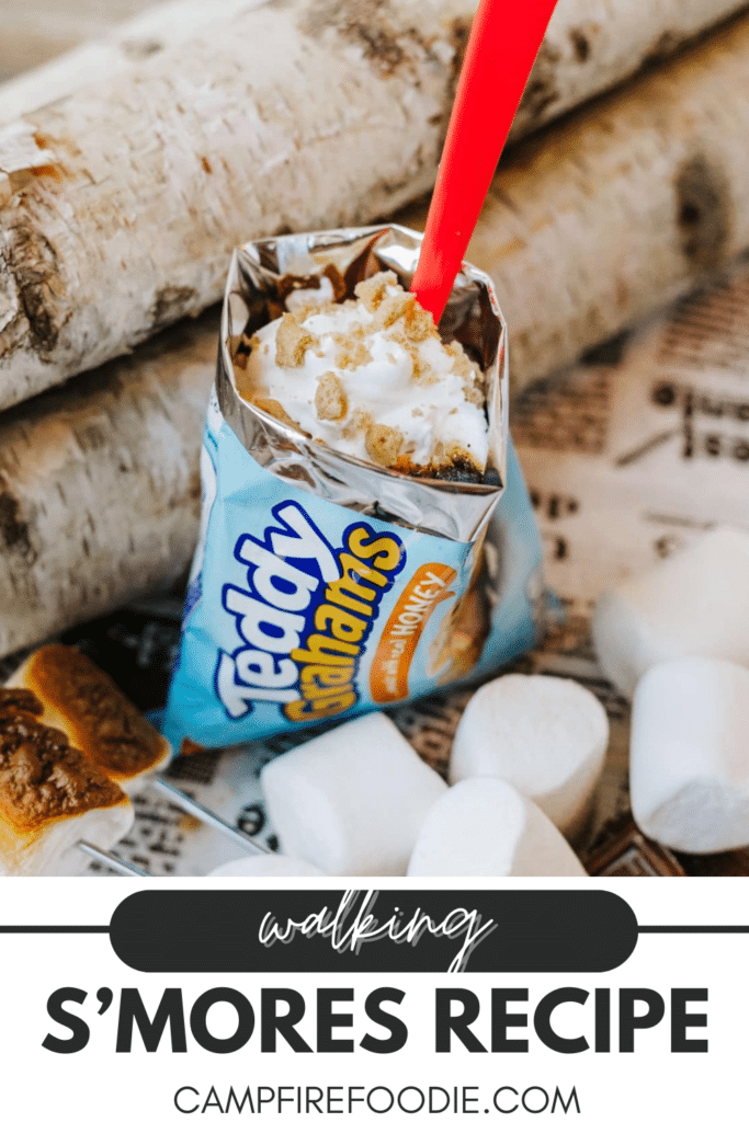 A bag of Teddy Grahams filled with whipped cream, chocolate, and graham cracker crumbs sits beside marshmallows and a s’more. Text reads, “Walking S’mores Recipe, campfirefoodie.com.”.
