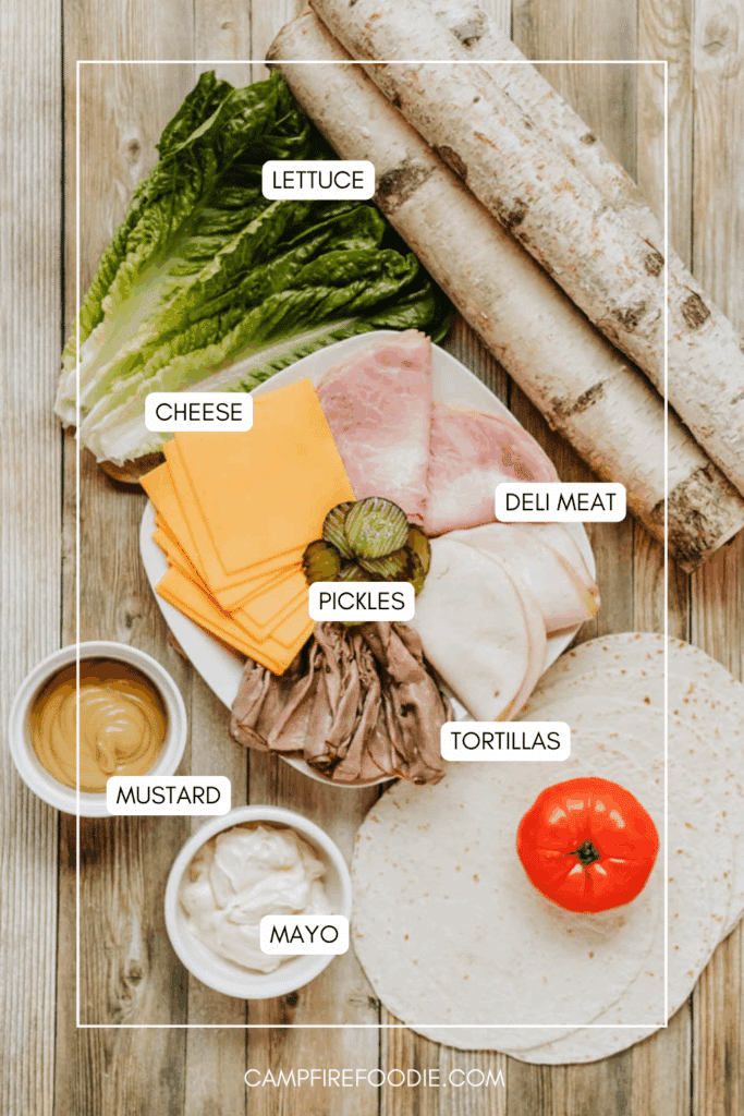 A flat lay of sandwich ingredients on a wooden surface: romaine lettuce, sliced cheese, deli meat, pickles, mayonnaise, mustard, a whole tomato, tortillas, and baguettes. Each item is labeled.