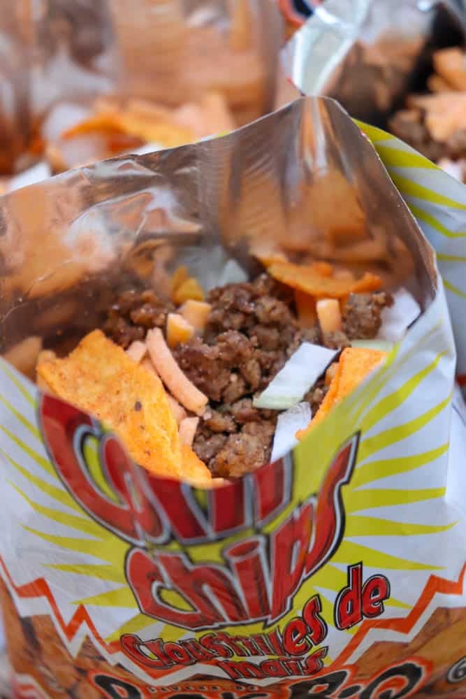 An open bag of corn chips filled with ground beef, diced onions, and cheese, resembling a walking taco.