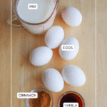 A measuring cup of milk, five white eggs, a small bowl of ground cinnamon, and a small bowl of vanilla extract arranged on a wooden surface. Labels indicate each ingredient.