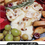 A skillet filled with melted brie cheese topped with chopped pecans and rosemary, surrounded by green grapes, sliced apples, and plums. Text overlay reads camping skillet brie recipe.