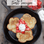 A cast iron skillet with three pieces of French toast topped with sliced strawberries and a dollop of whipped cream sits on a wooden table, next to bowls of more strawberries and whipped cream. Text reads: Camping Hack Easy French Toast Recipe.