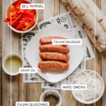 Top-down view of a plate with three Italian sausages, surrounded by bowls of sliced bell peppers, white onions, olive oil, Italian seasoning, and birch logs on a wooden surface. Labels identify each ingredient.
