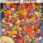 A colorful stir-fry with sliced sausage, diced potatoes, corn, red and green bell peppers, and onions, cooked on a griddle with two slices of toasted bread. Text reads Blackstone cowboy stir-fry campfirefoodie.com.