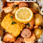 Foil packet filled with shrimp, sliced sausage, corn on the cob, potatoes, and a lemon slice, garnished with herbs and served with a fork. Text reads foil packet shrimp boil and campfirefoodie.com.