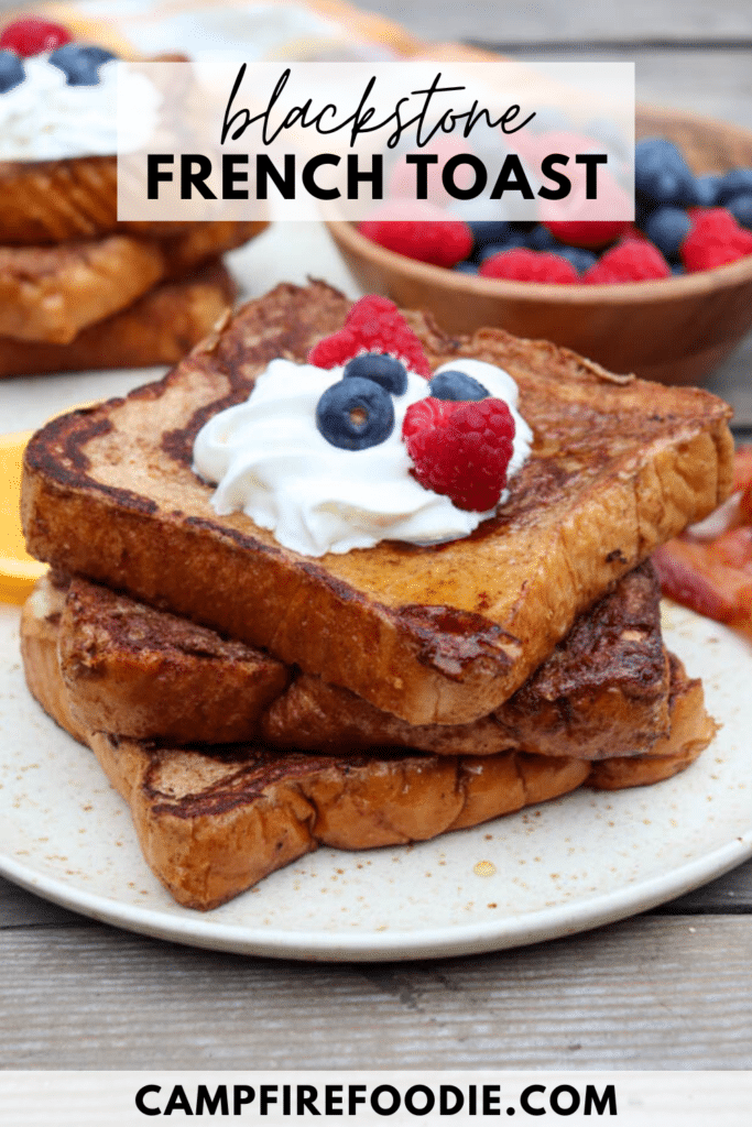 Three thick slices of French toast stacked on a plate, topped with whipped cream, blueberries, and raspberries. A bowl of mixed berries and orange slices are in the background. Text reads Blackstone French Toast.
