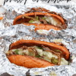 Two Philly cheesesteak sandwiches with melted cheese, grilled onions, and green peppers in toasted buns, wrapped in aluminum foil. Text reads “Blackstone Philly Cheesesteak” and “campfirefoodie.com.”.