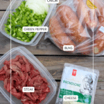 Plastic containers with sliced onion and green pepper, a pack of soft buns, raw sliced steak, and a package of provolone cheese arranged on a wooden surface. Each item is labeled.