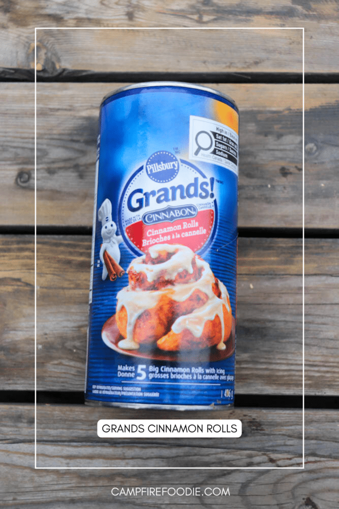 A can of Pillsbury Grands! Cinnabon Cinnamon Rolls is placed on a wooden surface. The label shows iced cinnamon rolls and the Pillsbury Doughboy mascot. Text: Grands Cinnamon Rolls.
