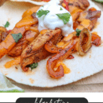 Close-up of chicken fajitas on tortillas, topped with sautéed peppers, onions, melted cheese, a dollop of sour cream, and cilantro, with lime slices on the side. Text reads: blackstone chicken fajitas campfirefoodie.com.