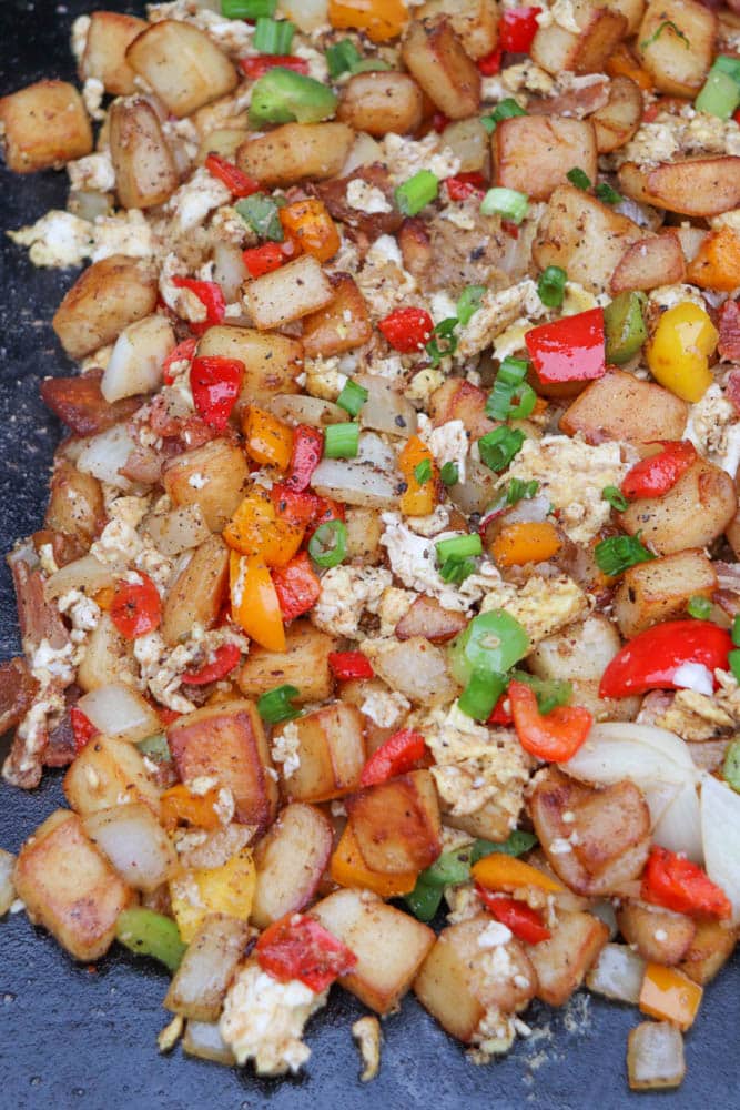 A close-up of diced, pan-fried potatoes mixed with scrambled eggs, bell peppers, onions, and green onions, all seasoned and cooked together. The mixture appears colorful and appetizing.