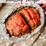 An overhead view of a foil-wrapped meatloaf topped with tomato sauce on a wooden board, surrounded by diced onions and a red checkered cloth. Text reads: Foil Packet Meatloaf Recipe and campfirefoodie.com.