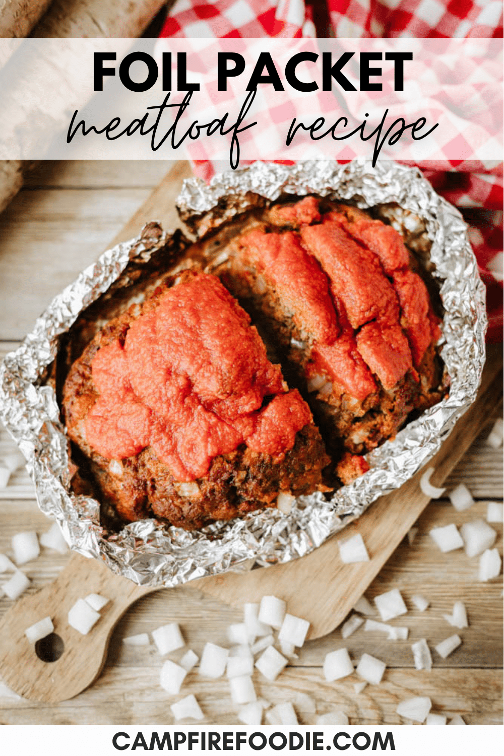 An overhead view of a foil-wrapped meatloaf topped with tomato sauce on a wooden board, surrounded by diced onions and a red checkered cloth. Text reads: Foil Packet Meatloaf Recipe and campfirefoodie.com.