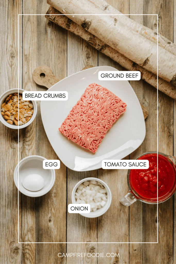 Overhead view of a plate with raw ground beef, surrounded by bowls containing bread crumbs, a whole egg, chopped onion, and tomato sauce on a wooden surface. Each ingredient is labeled.