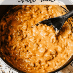 A black Dutch oven filled with creamy chili mac and a black spoon, with Dutch Oven Chili Mac text above. The image is branded with campfirefoodie.com at the bottom.