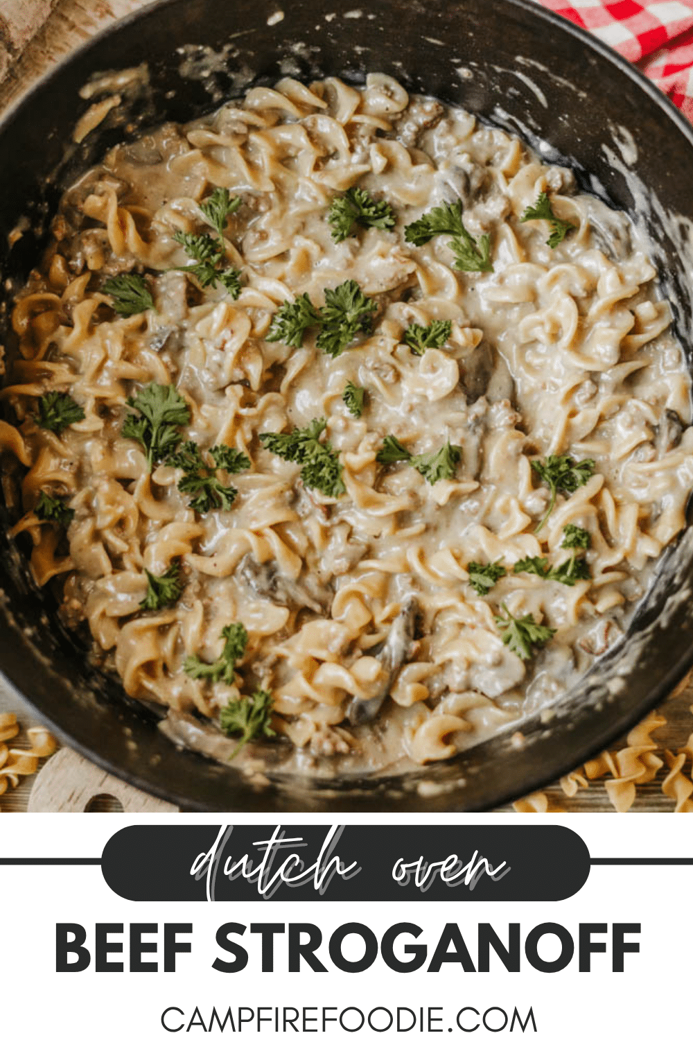 A Dutch oven filled with creamy beef stroganoff noodles, garnished with fresh parsley. The text at the bottom reads Dutch Oven Beef Stroganoff campfirefoodie.com.