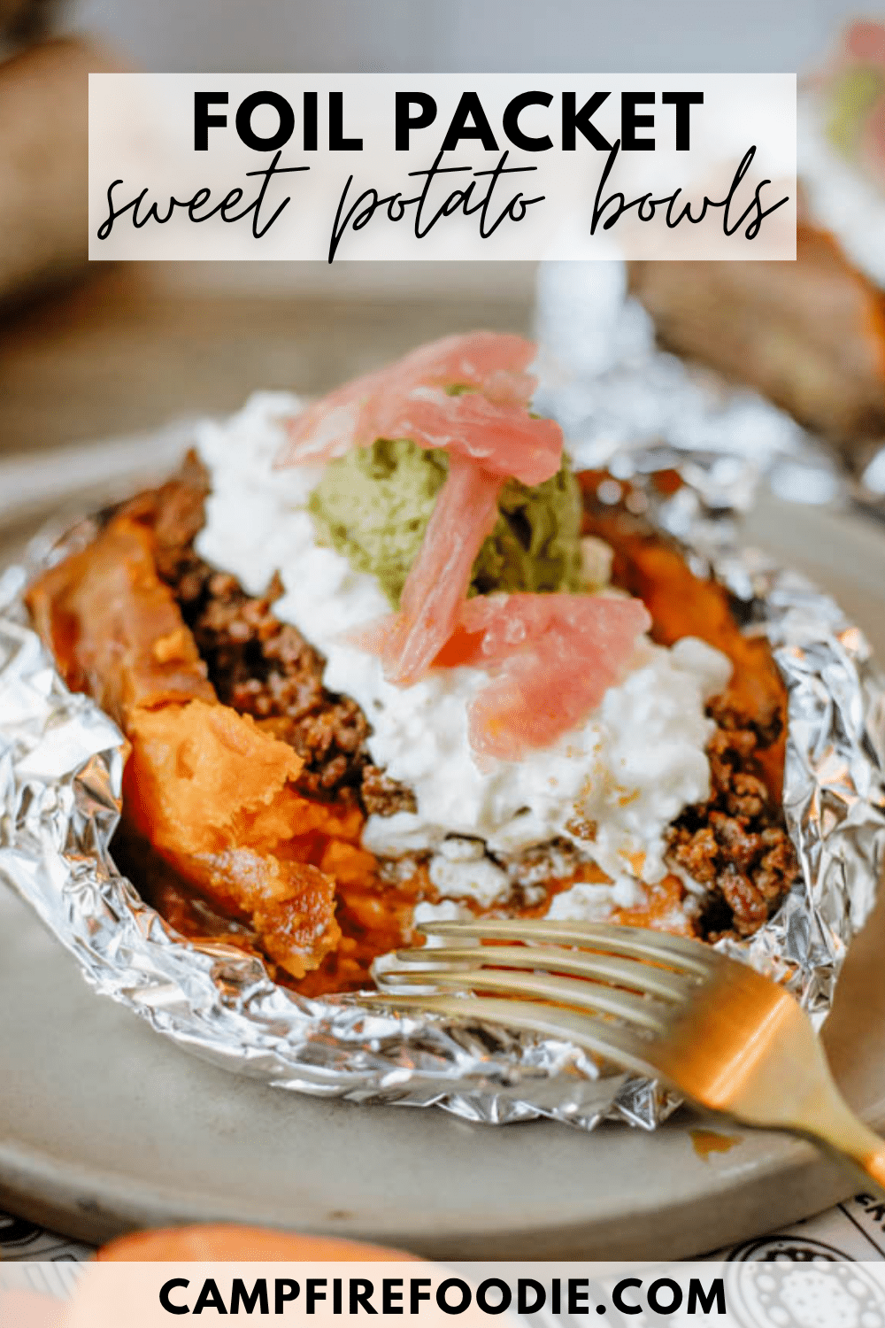 A baked sweet potato served in foil, topped with ground meat, cottage cheese, guacamole, and pickled onions, with a fork on the plate. Text reads Foil Packet Sweet Potato Bowls and campfirefoodie.com.