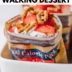 A 100-calorie snack bag is filled with whipped cream, sliced strawberries, and pretzel pieces, creating a strawberry pretzel walking dessert. The image is labeled “STRAWBERRY PRETZEL WALKING DESSERT.”.
