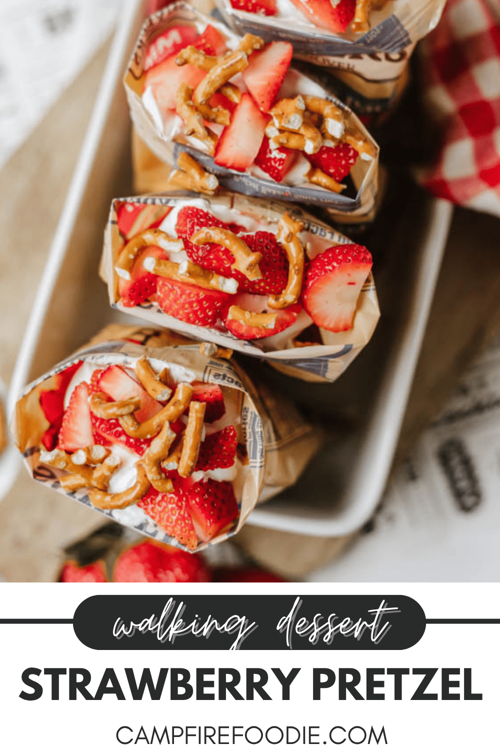 Three paper snack bags filled with layers of strawberries, pretzels, and cream are displayed on a tray, with text reading “walking dessert Strawberry Pretzel campfirefoodie.com” at the bottom.