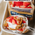 A spoonful of strawberry pretzel walking dessert with whipped cream, sliced strawberries, and pretzels, above an open snack bag. Text reads strawberry pretzel walking dessert and campfirefoodie.com.